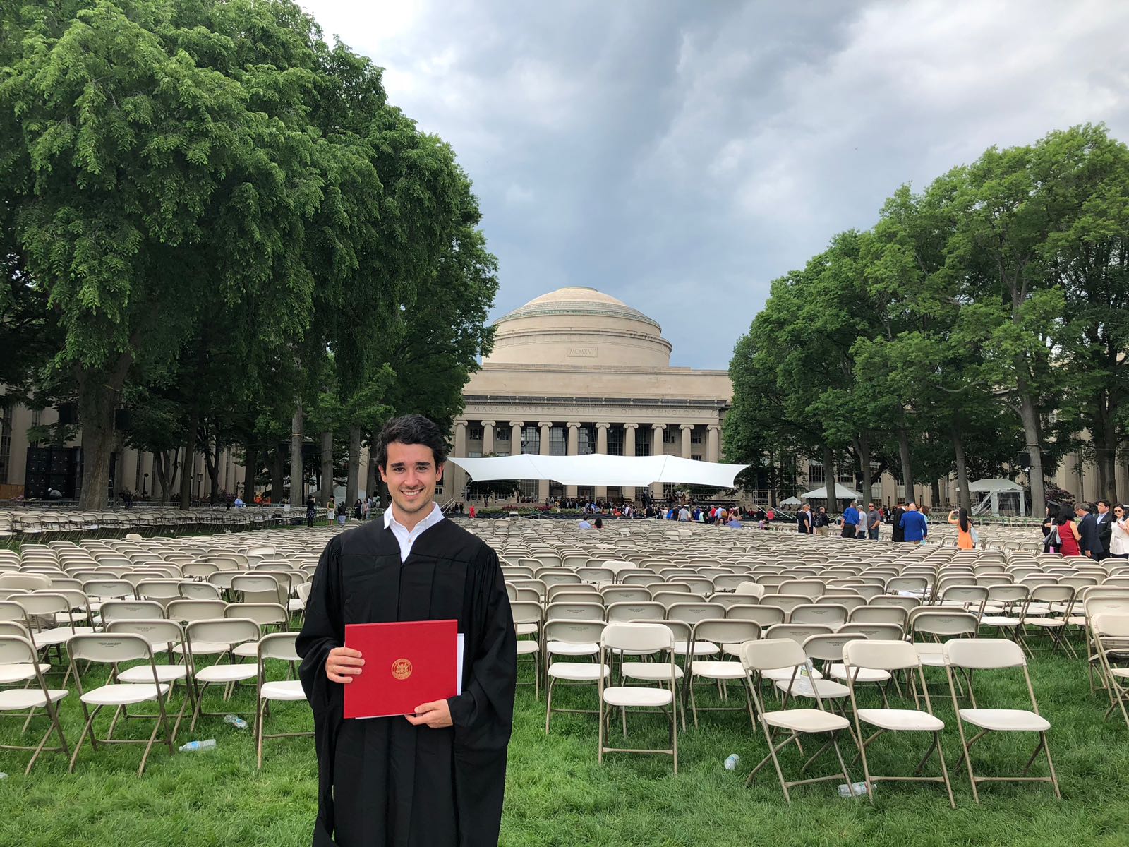 Carlos Muñoz Royo fotografiado con su Título y el campous del Massachusetts Institute of Technology al fondo el día de su graduación.